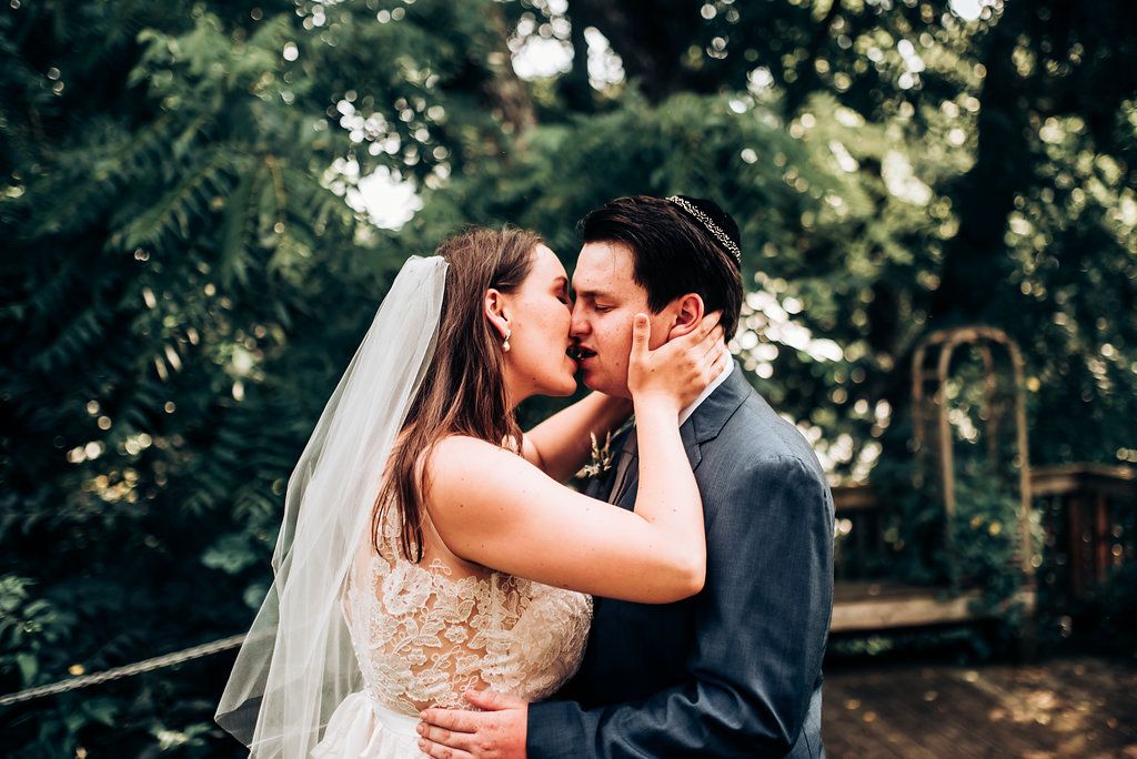 Intimate wedding kiss captured in a lush garden setting.