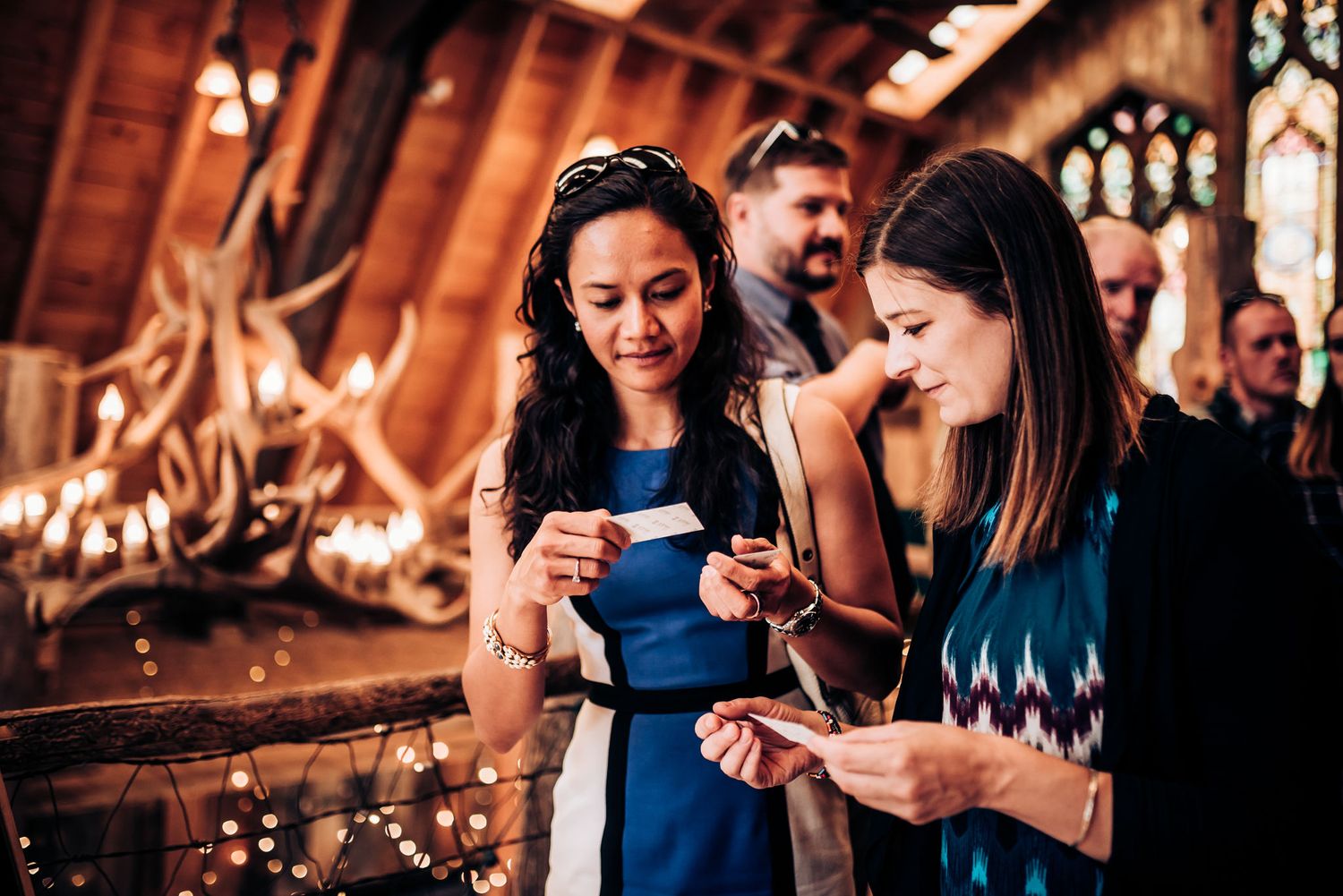 People gathered at an indoor event with string lights and rustic wooden decor.