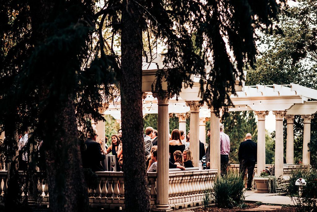 Classical columned venue with trees framing guests gathering on a stone terrace.