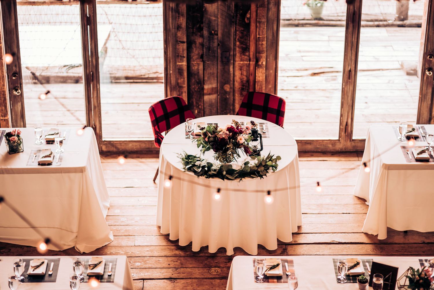 Round sweetheart table with white tablecloth and floral centerpiece in rustic wooden venue.