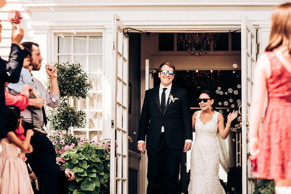 Couple exiting venue through white French doors as guests celebrate.