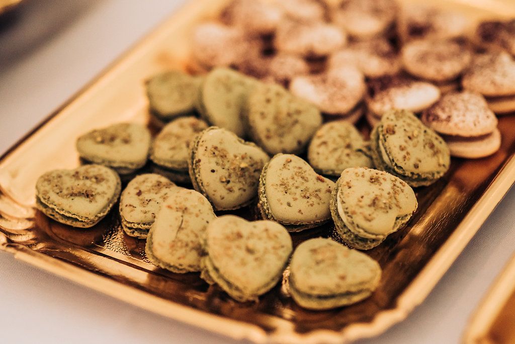 Heart-shaped green macarons arranged on a gold serving tray at a dessert table.