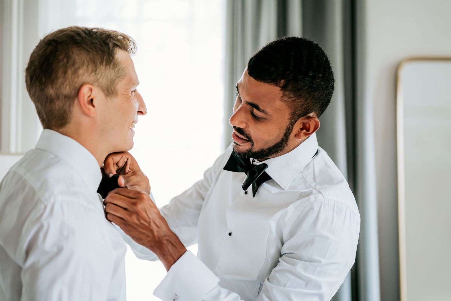 Two people helping each other adjust their bow ties while getting ready.