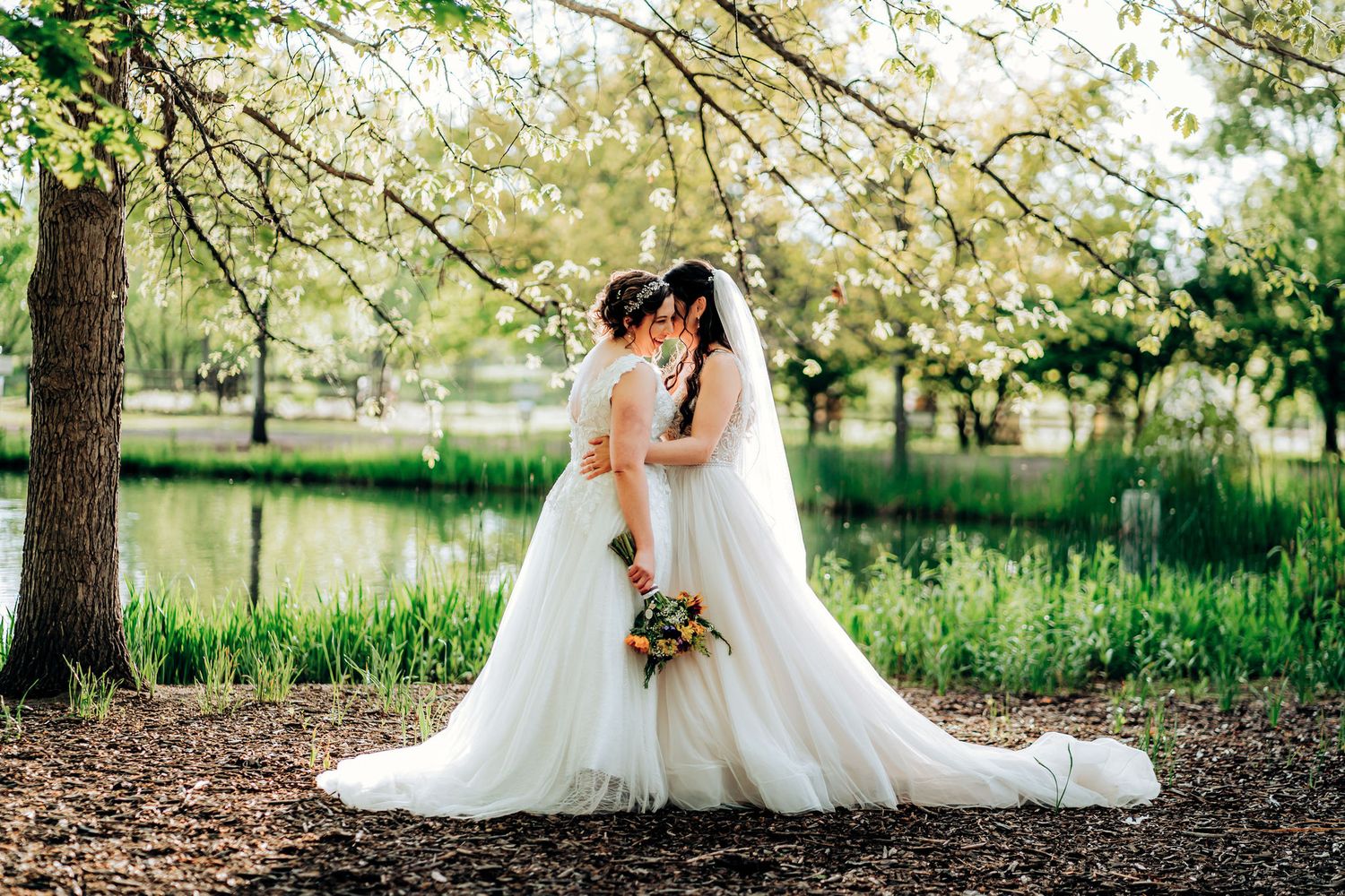 Romantic wedding portrait under blooming spring trees near pond.