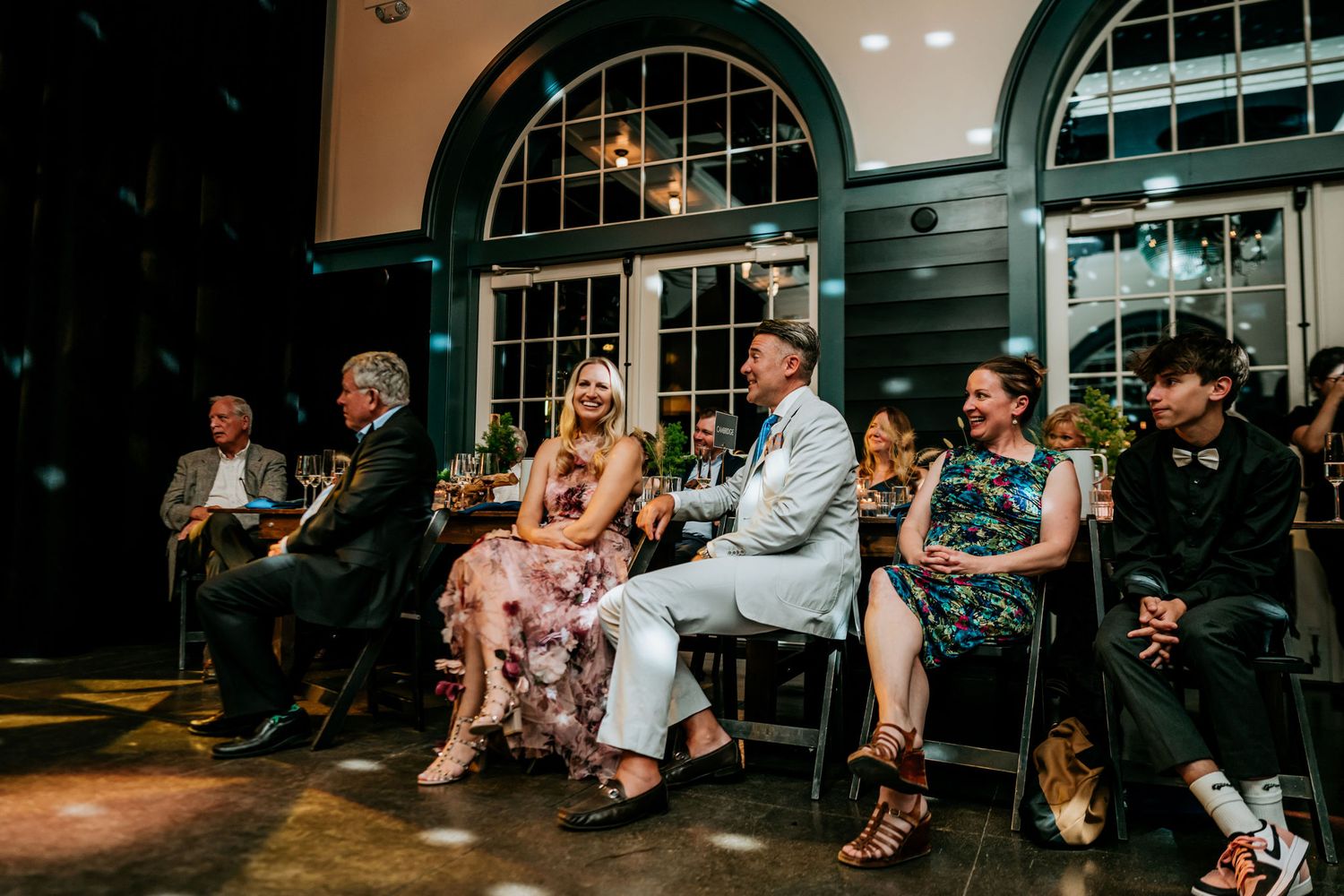 Row of attendees seated in an elegant venue with arched windows during an evening event.
