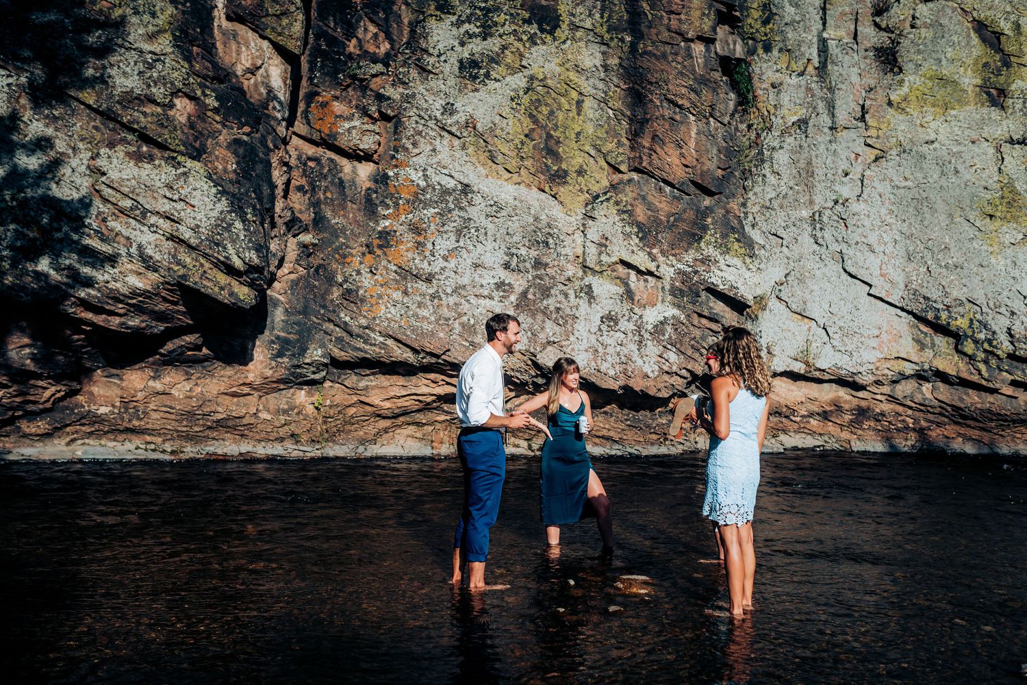 People standing in shallow water against dramatic rocky cliff backdrop.