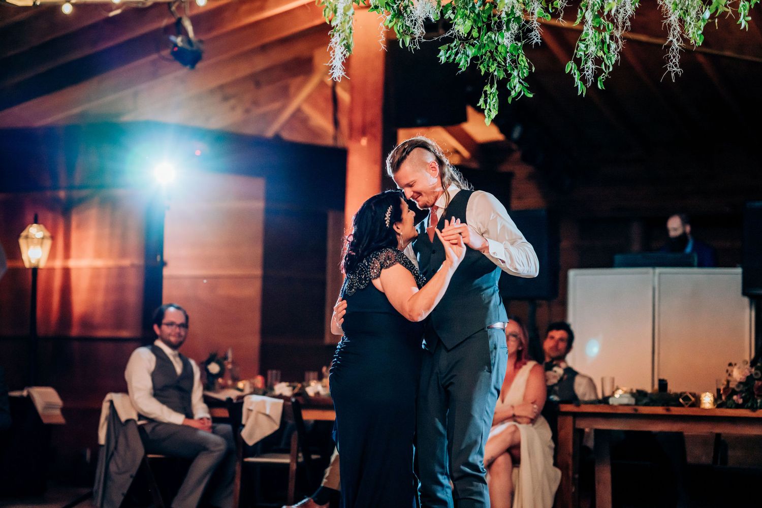 A couple shares an intimate slow dance at their reception under warm lighting.