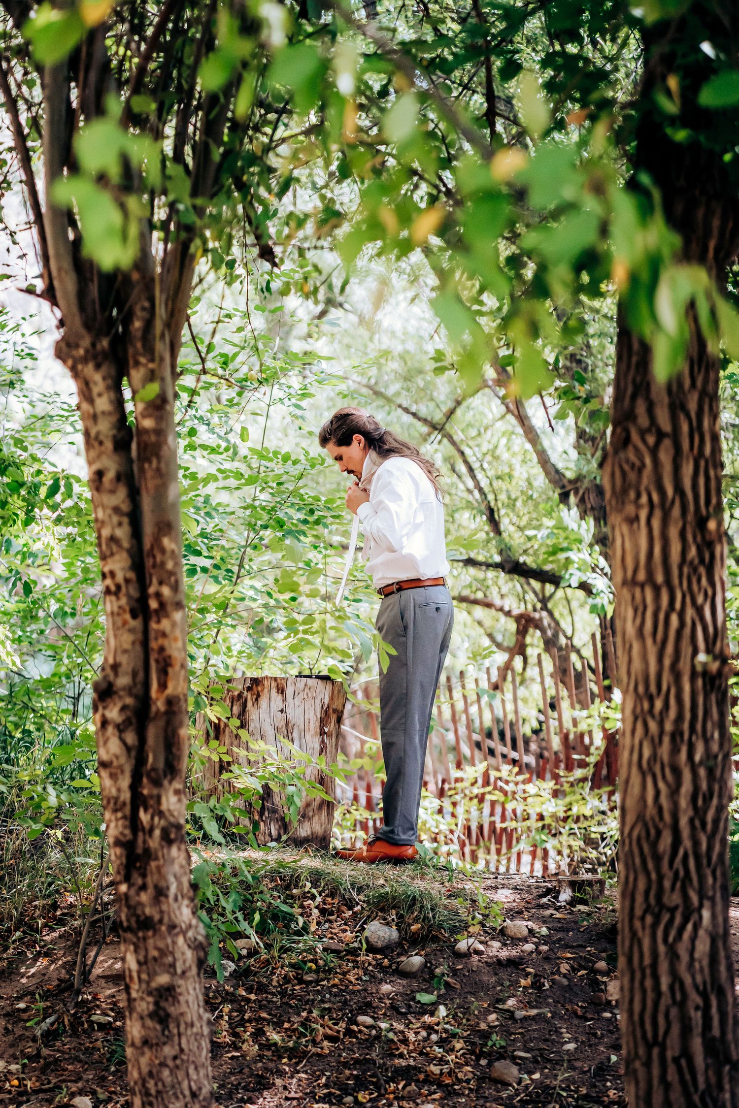 Figure standing on log in lush green forest setting wearing formal attire.
