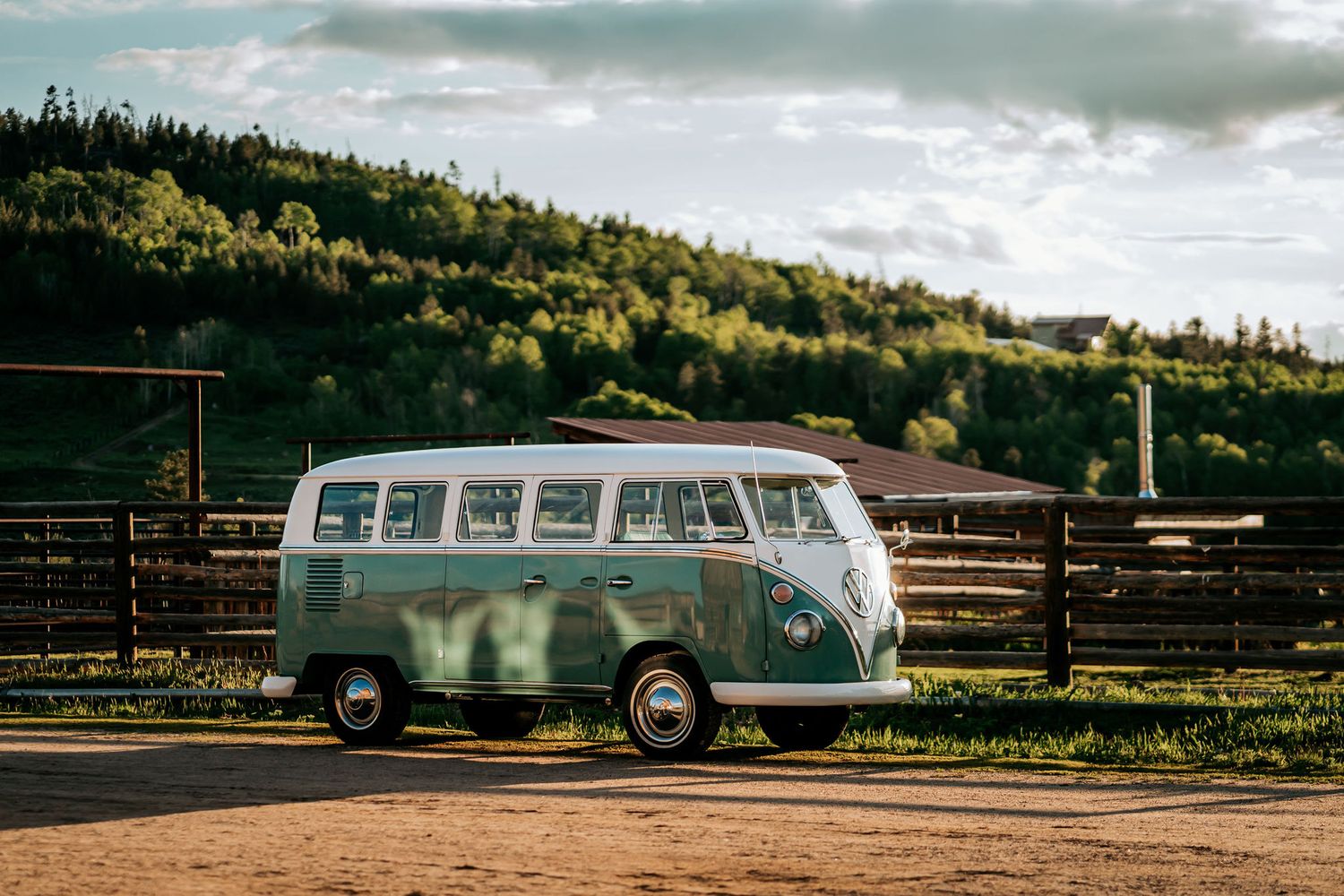 Classic vintage Volkswagen bus parked in front of green rolling hills at sunset.