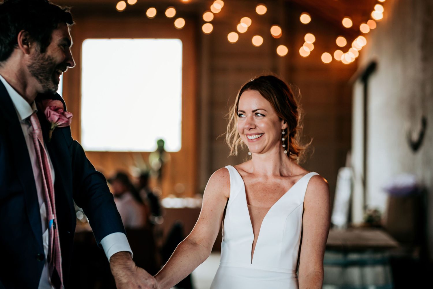 A joyful wedding dance moment captured under string lights in a rustic venue.