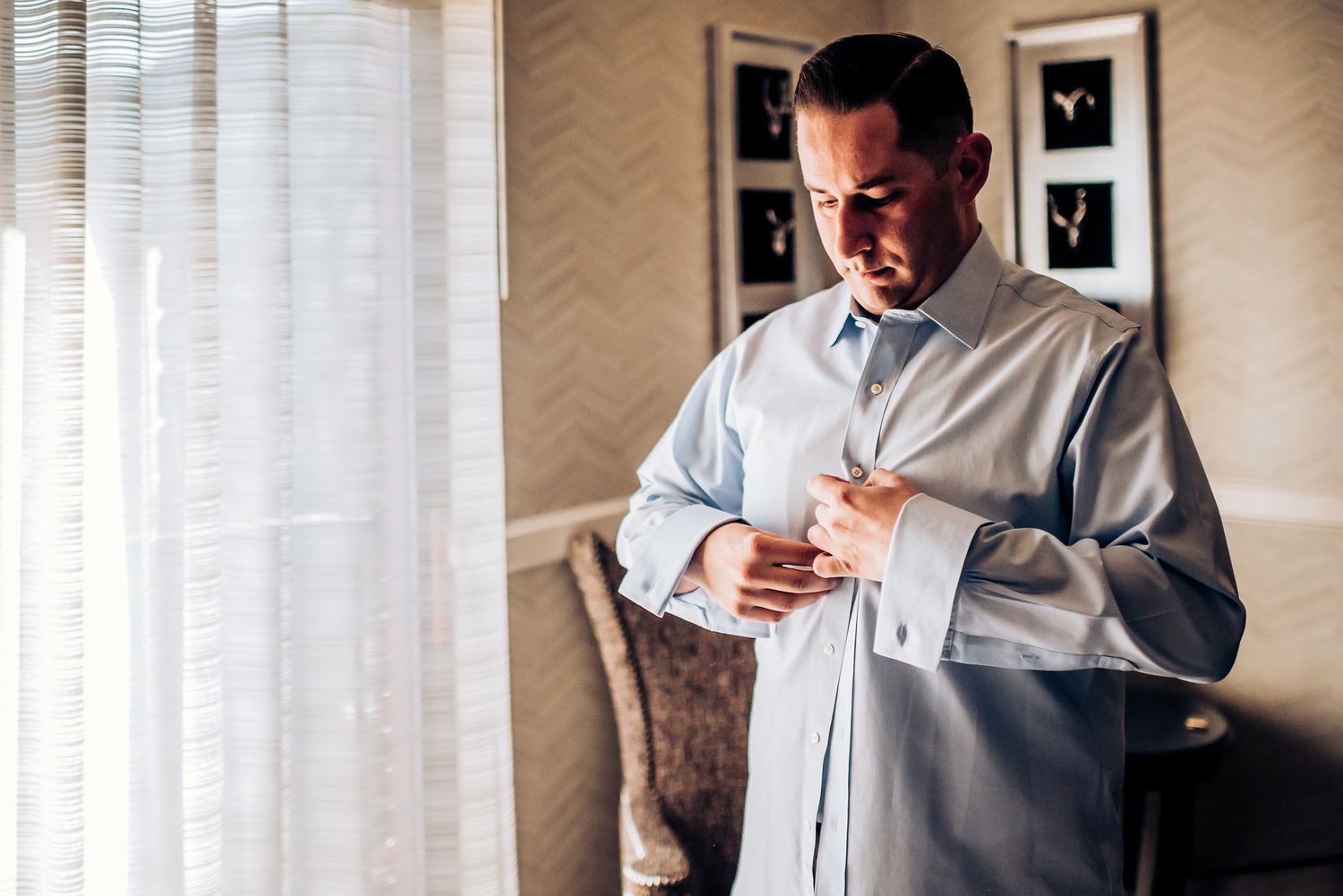 Someone in a white dress shirt prepares for a formal event near a sunlit window.