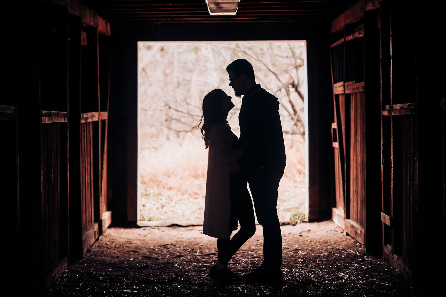 Silhouetted figures stand in loving embrace at a bright barn doorway.