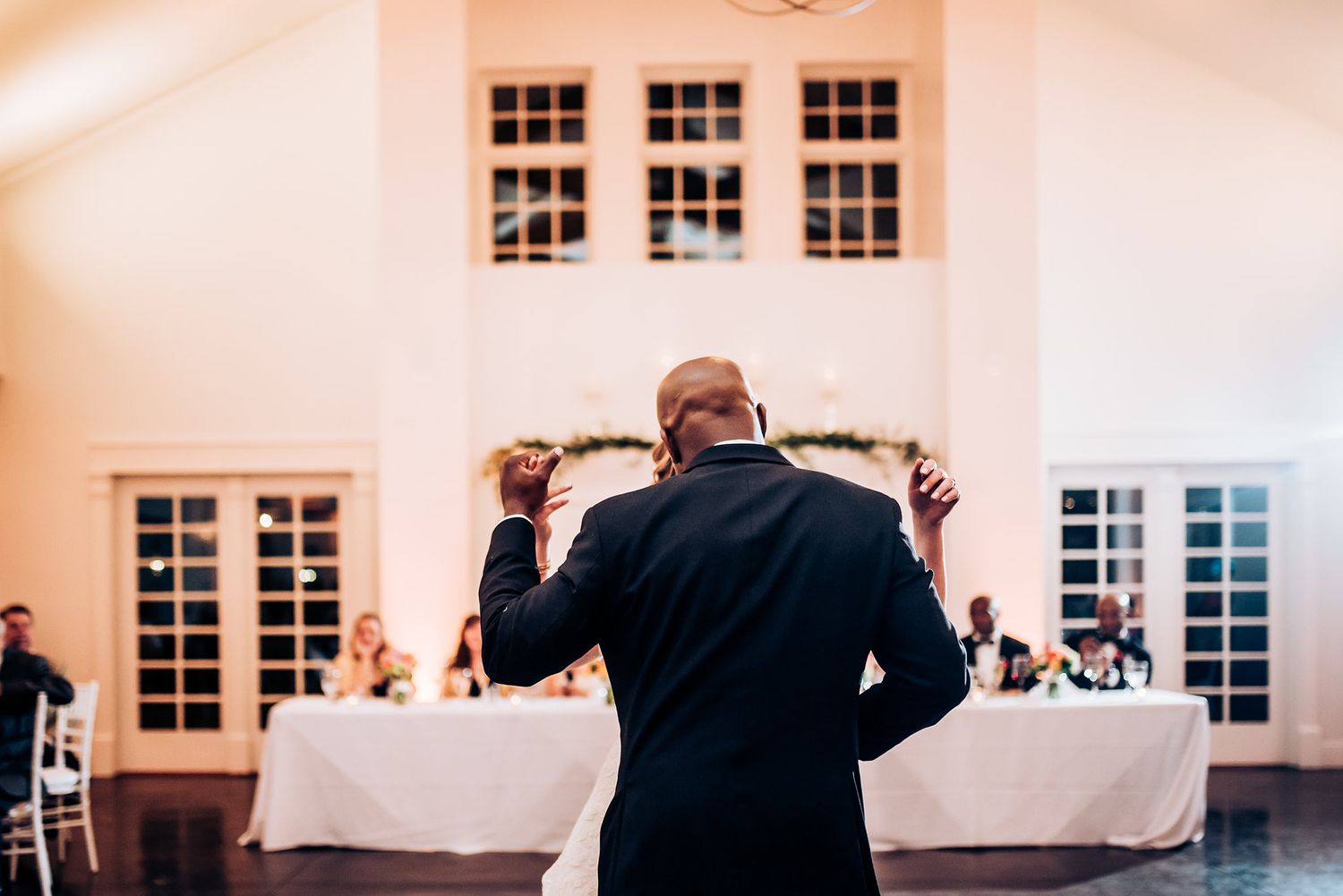 Speaker addresses wedding reception guests from behind podium in elegant venue.