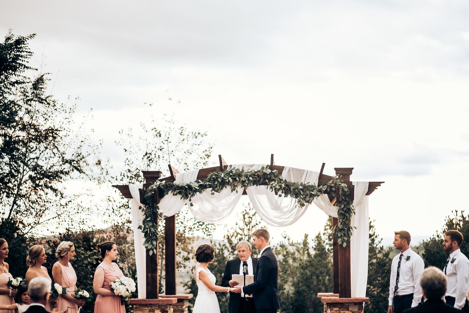 Wedding celebration outdoors as confetti rains down over a decorated wooden arch during the ceremony.