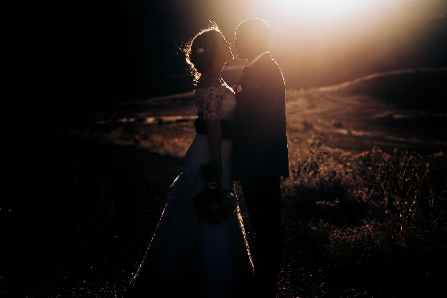 Wedding couple silhouetted against dramatic sunset light on a mountain path.