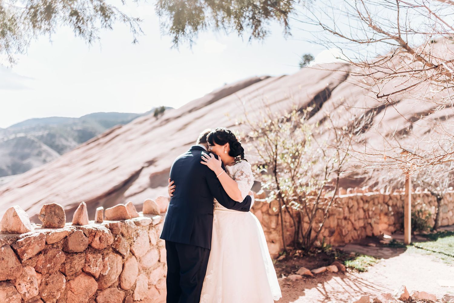 A romantic wedding embrace against red rock formations and desert landscape during an outdoor ceremony.