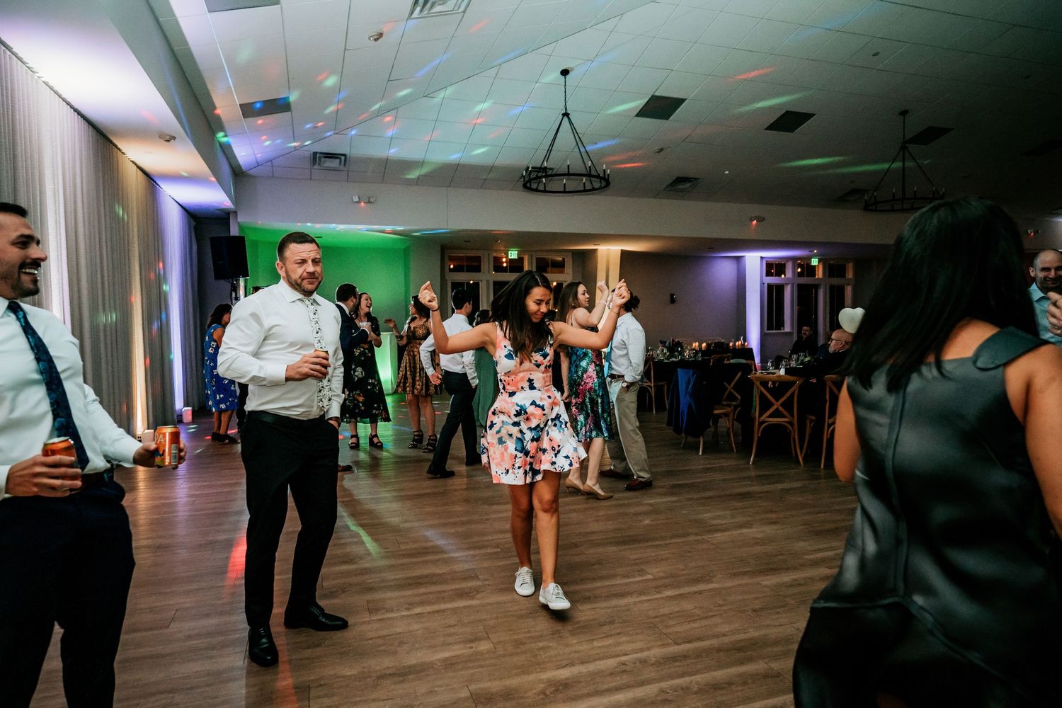 Couple dancing together at a wedding reception with colorful lighting and guests in the background.