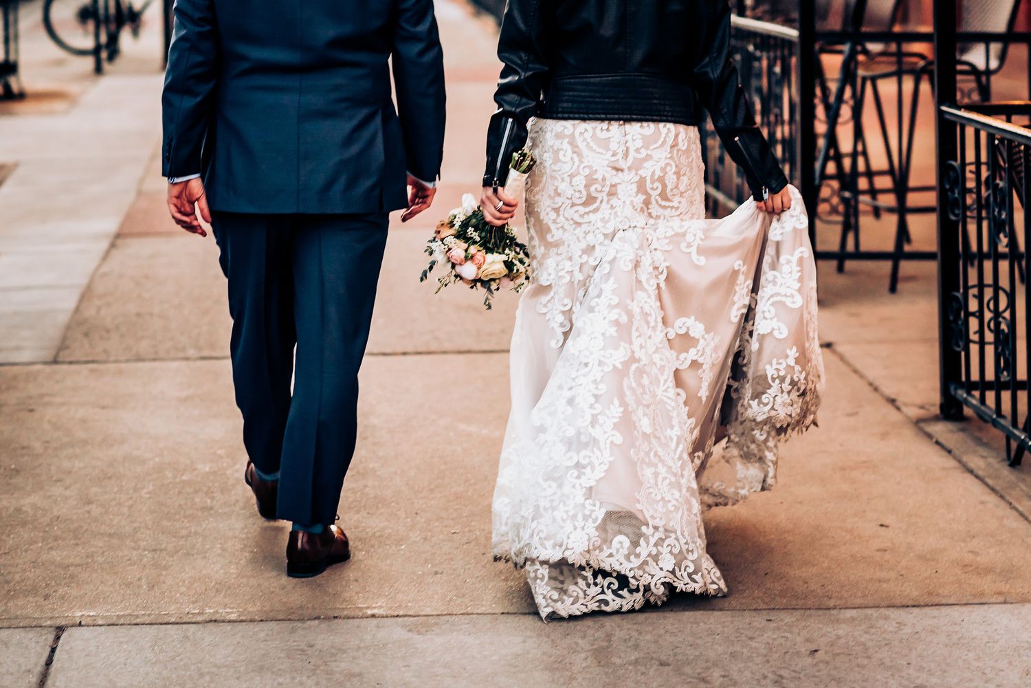 Close-up of bride in lace dress and groom walking on city sidewalk.