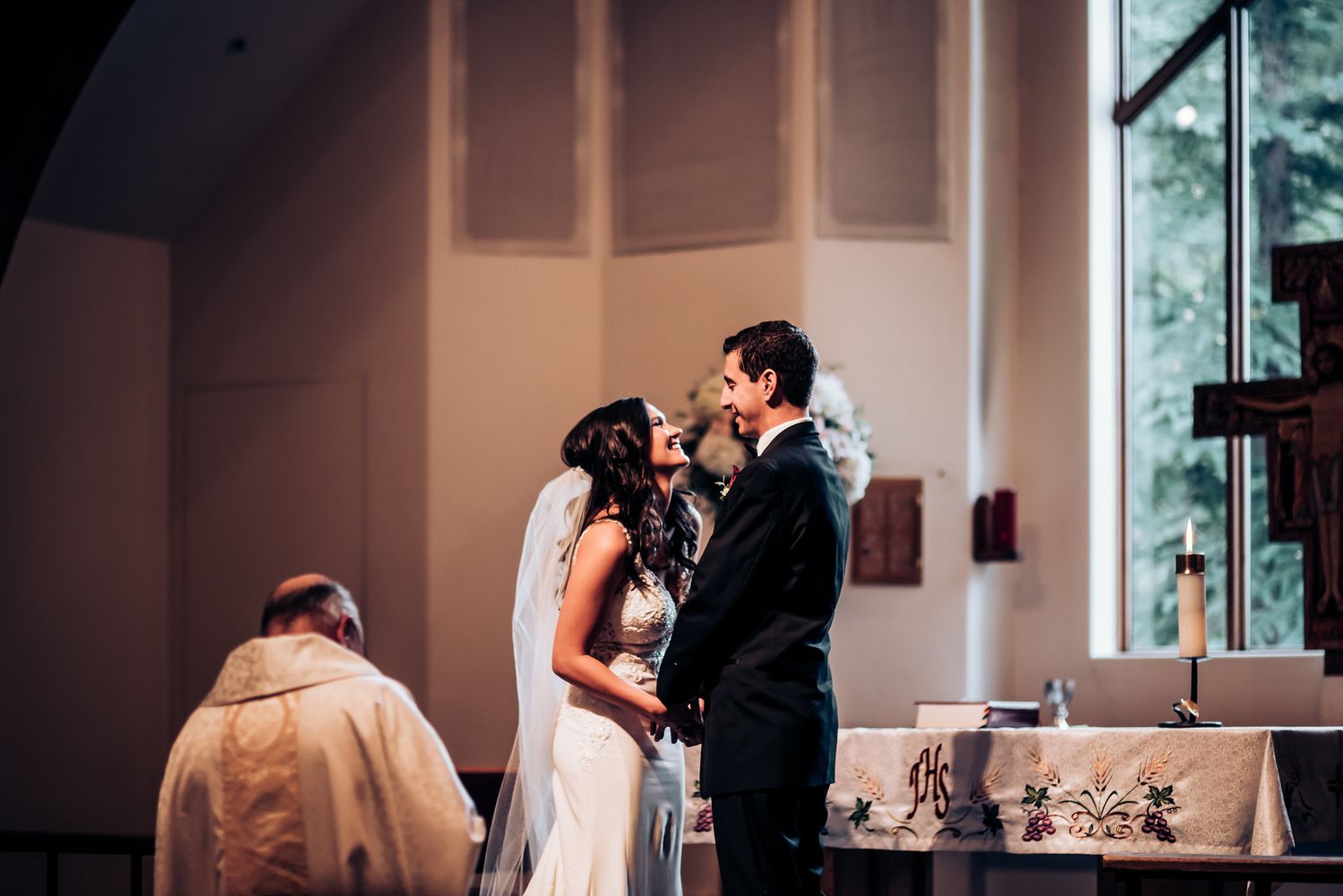 A tender moment during a church wedding ceremony with priest observing.