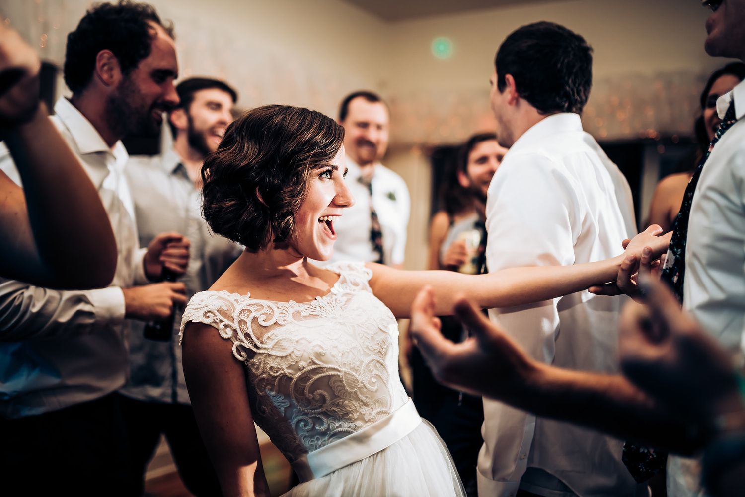 Dancer in lace wedding dress spins on crowded dance floor during reception celebration.