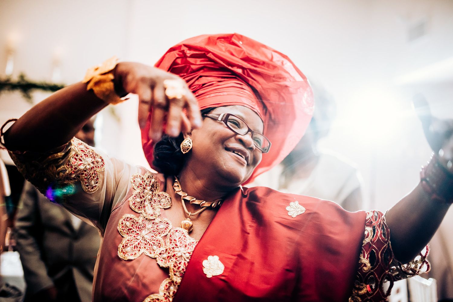 Guest in red traditional headwrap and dress dances enthusiastically at wedding celebration.