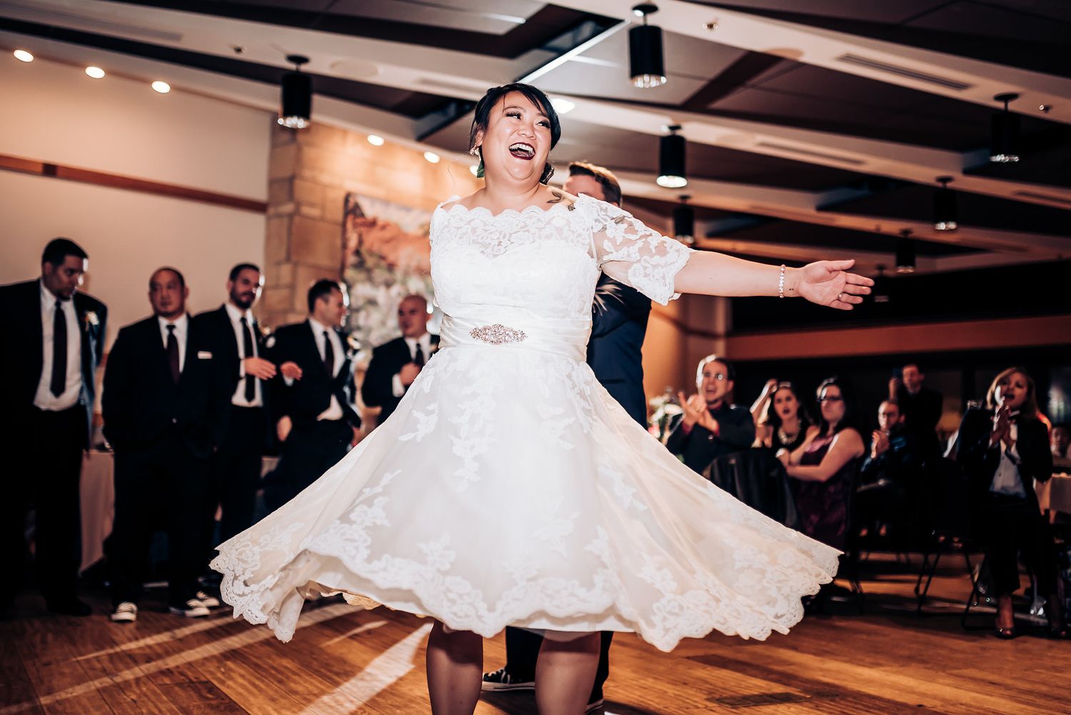 A bride in a lace dress twirls joyfully during a wedding reception dance.