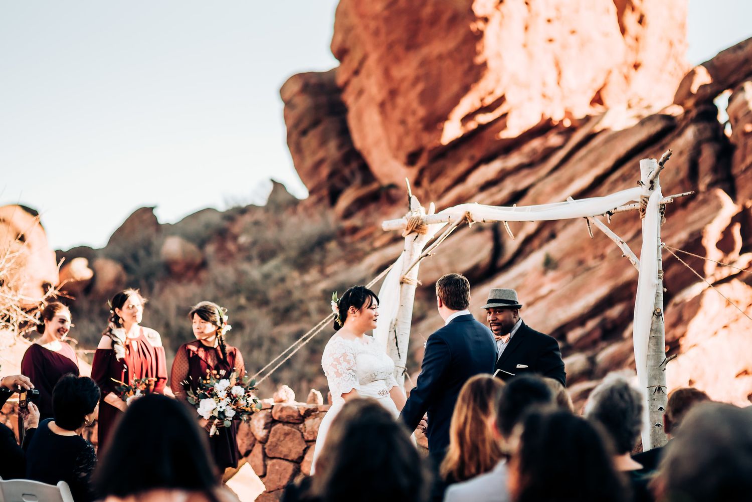 Wedding guests gather under a rustic wooden arch against stunning red rock formations.