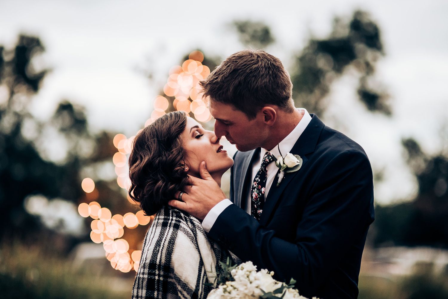 Intimate outdoor portrait with soft bokeh lights in background.