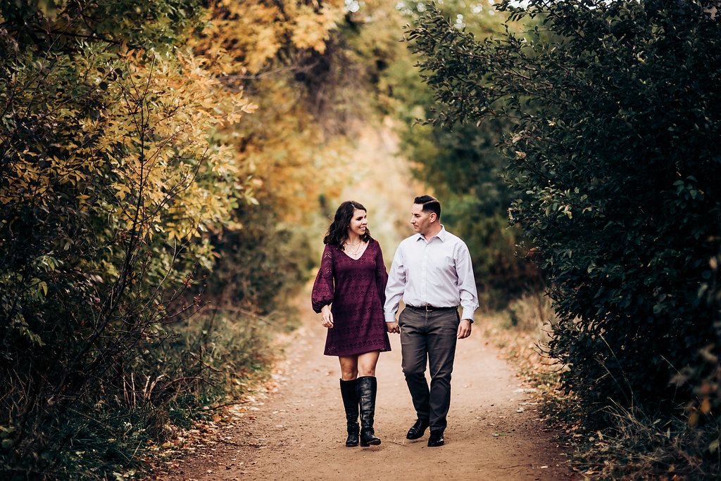 Couple walking hand in hand on autumn path surrounded by golden trees.
