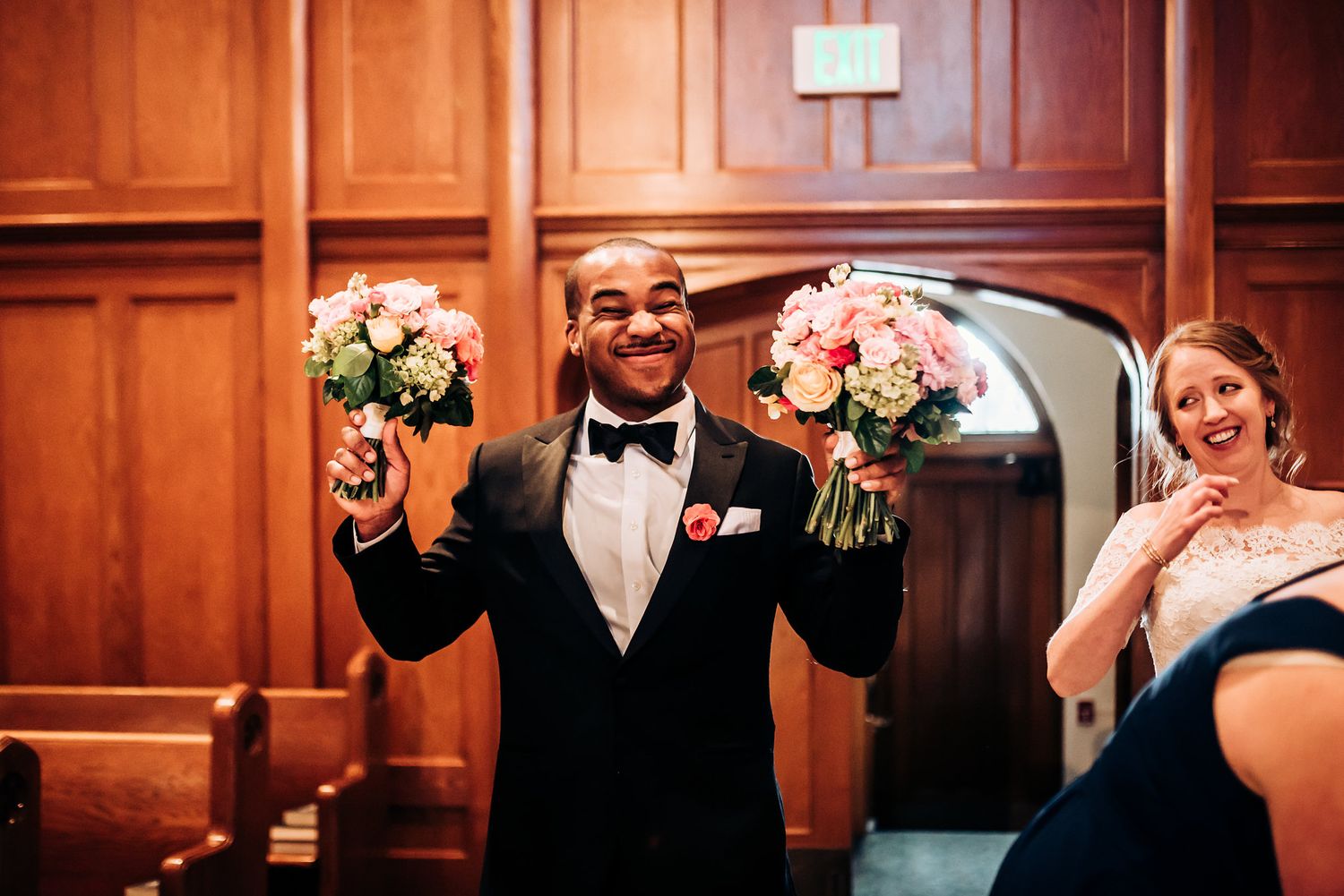 A joyful moment during a wedding celebration with bouquets held high in an elegant wood-paneled room.