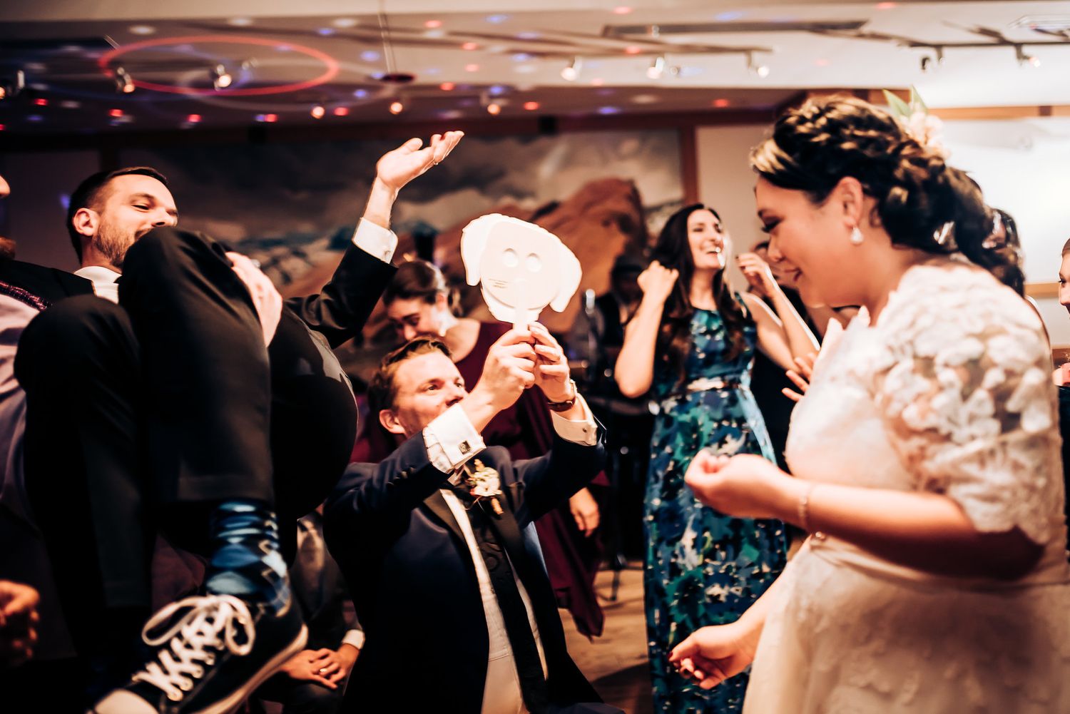 Wedding celebration with guests dancing and celebrating in a dimly lit reception hall.
