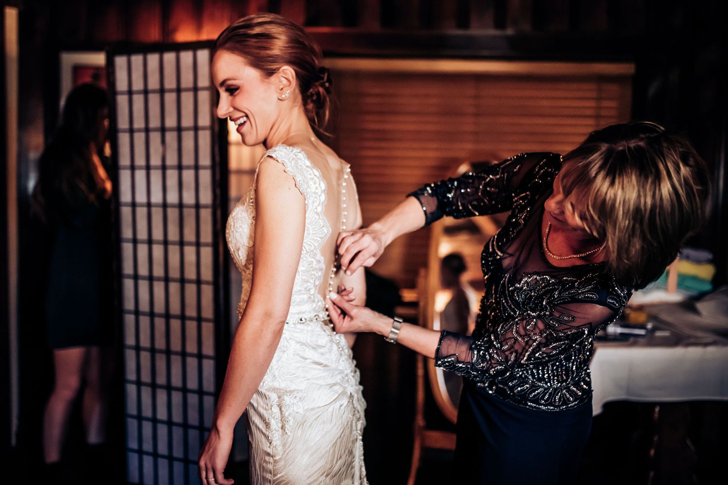 Helper adjusting the back of an elegant lace wedding dress during bridal preparations.