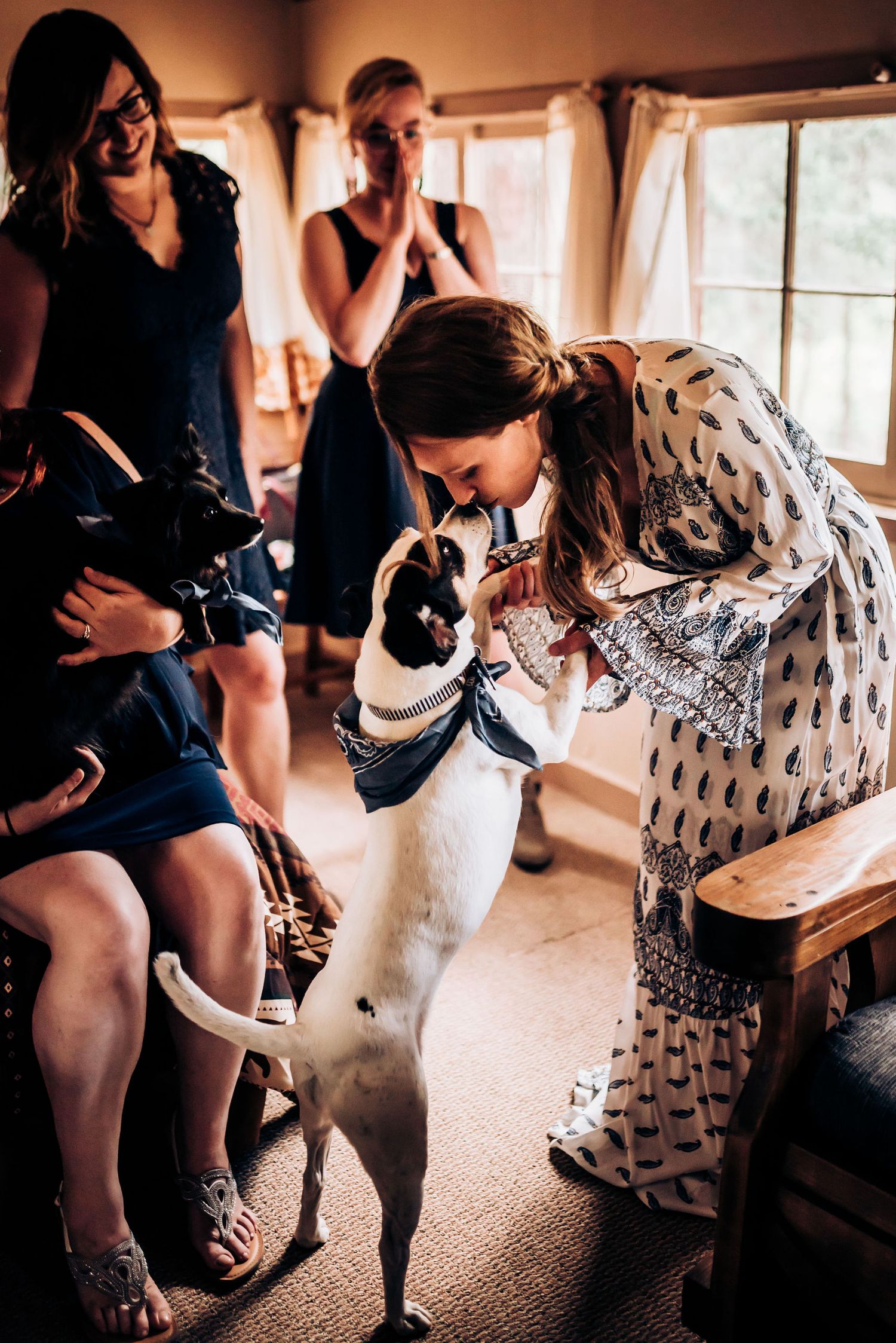A person in a patterned dress greets an excited white and black dog while others look on.