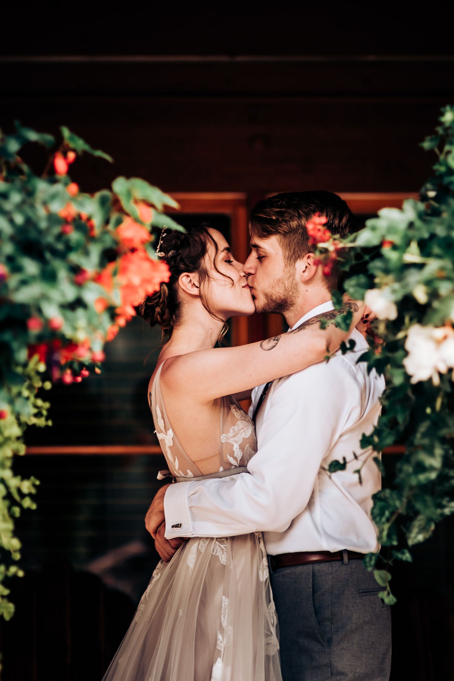A romantic kiss between newlyweds surrounded by flowering vines and soft lighting.
