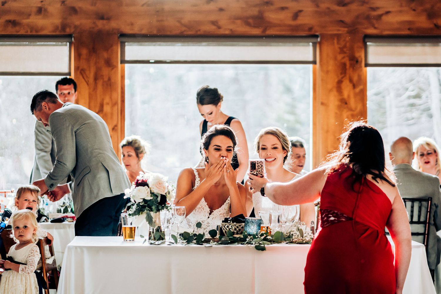 Candid reception moment captured at wedding dinner with wood-framed windows.