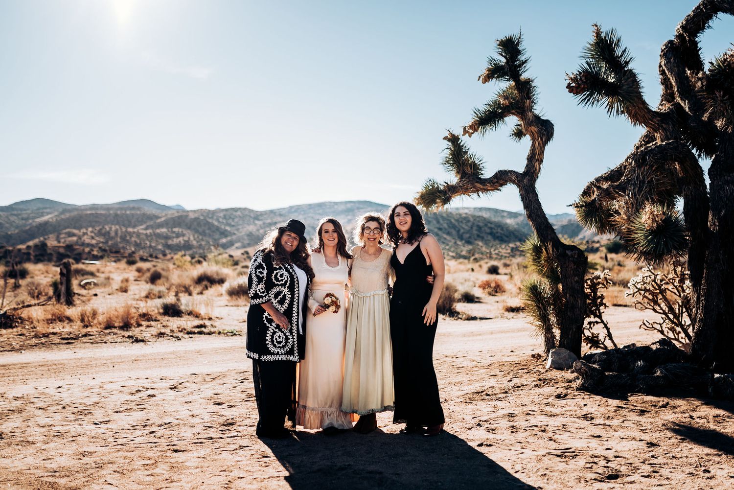Small group poses together against stunning desert landscape with Joshua tree and mountains.