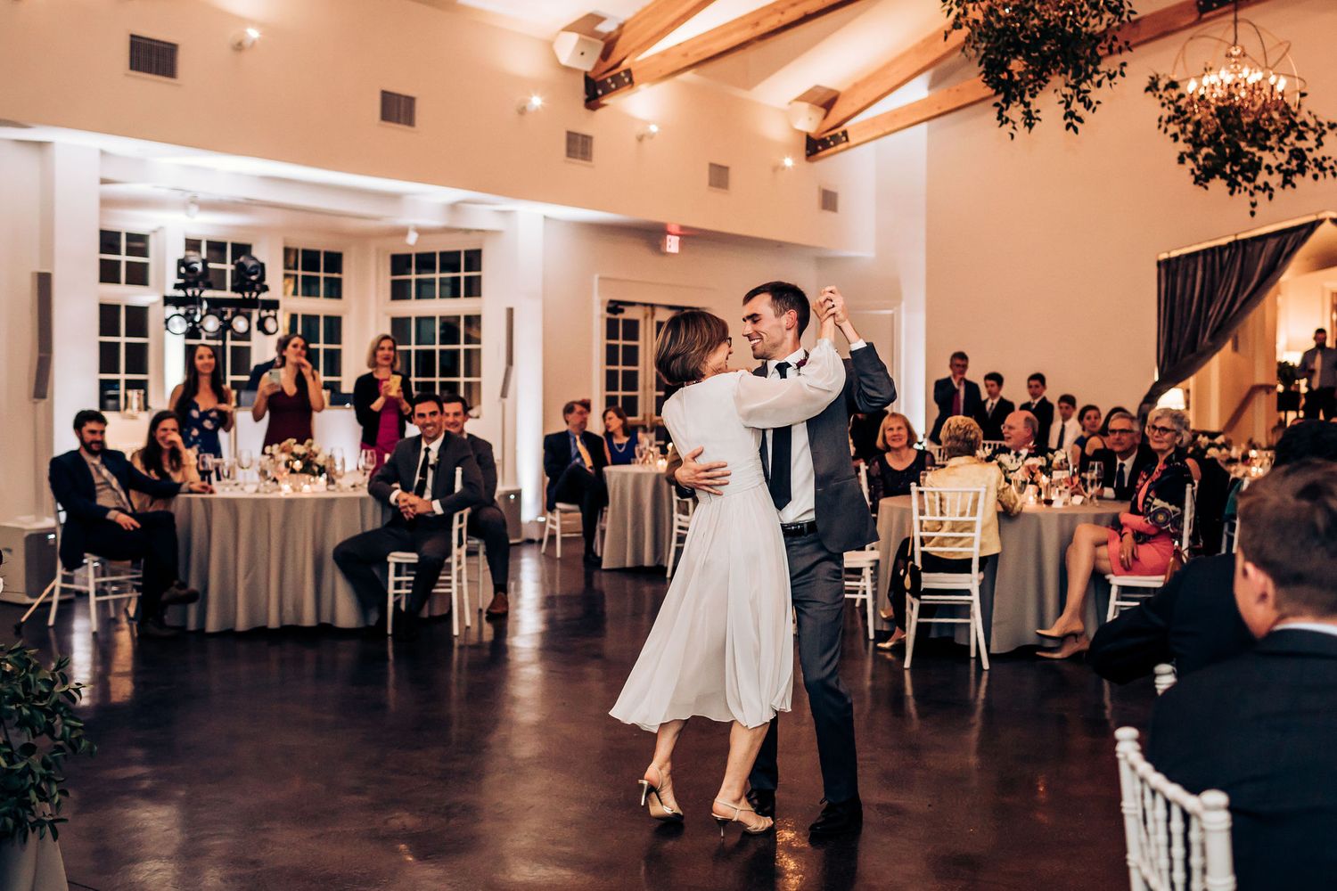 Couples dancing during a wedding reception in an elegant ballroom with exposed beams.