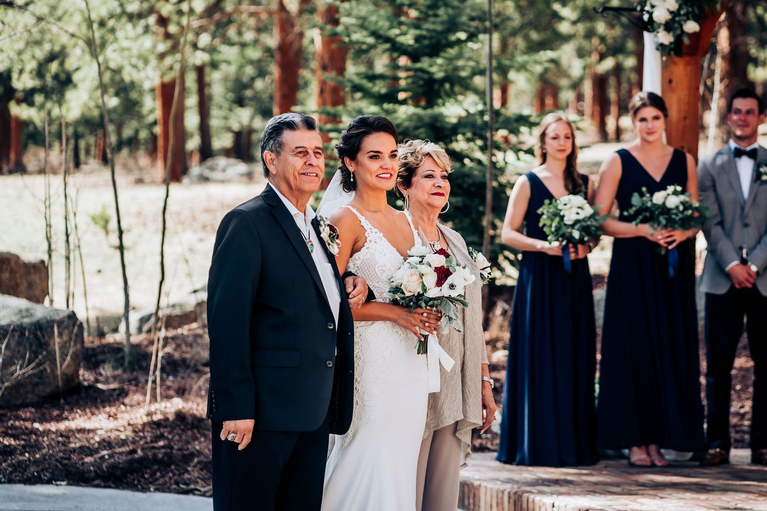 Wedding party in formal attire standing together during outdoor mountain ceremony.