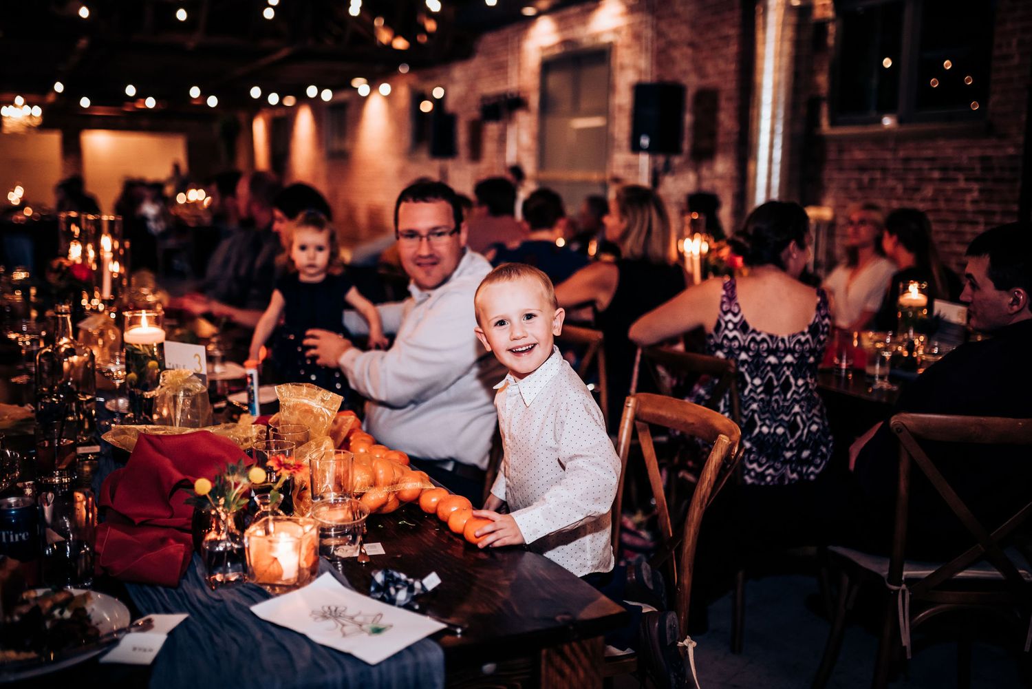 Candlelit dinner tables at a reception with string lights and brick walls creating an intimate atmosphere.