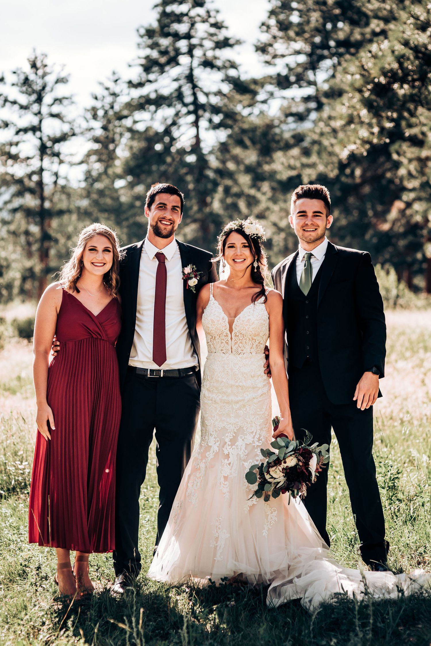 Wedding party members pose together outdoors in formal attire against a mountain backdrop.