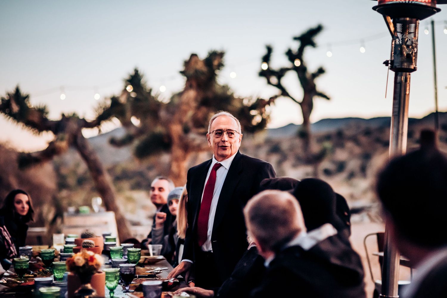 Desert dining event with string lights and Joshua trees in background at dusk.
