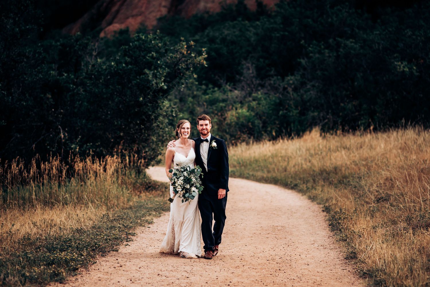 A couple walks together on a scenic trail with red rock formations in the background.