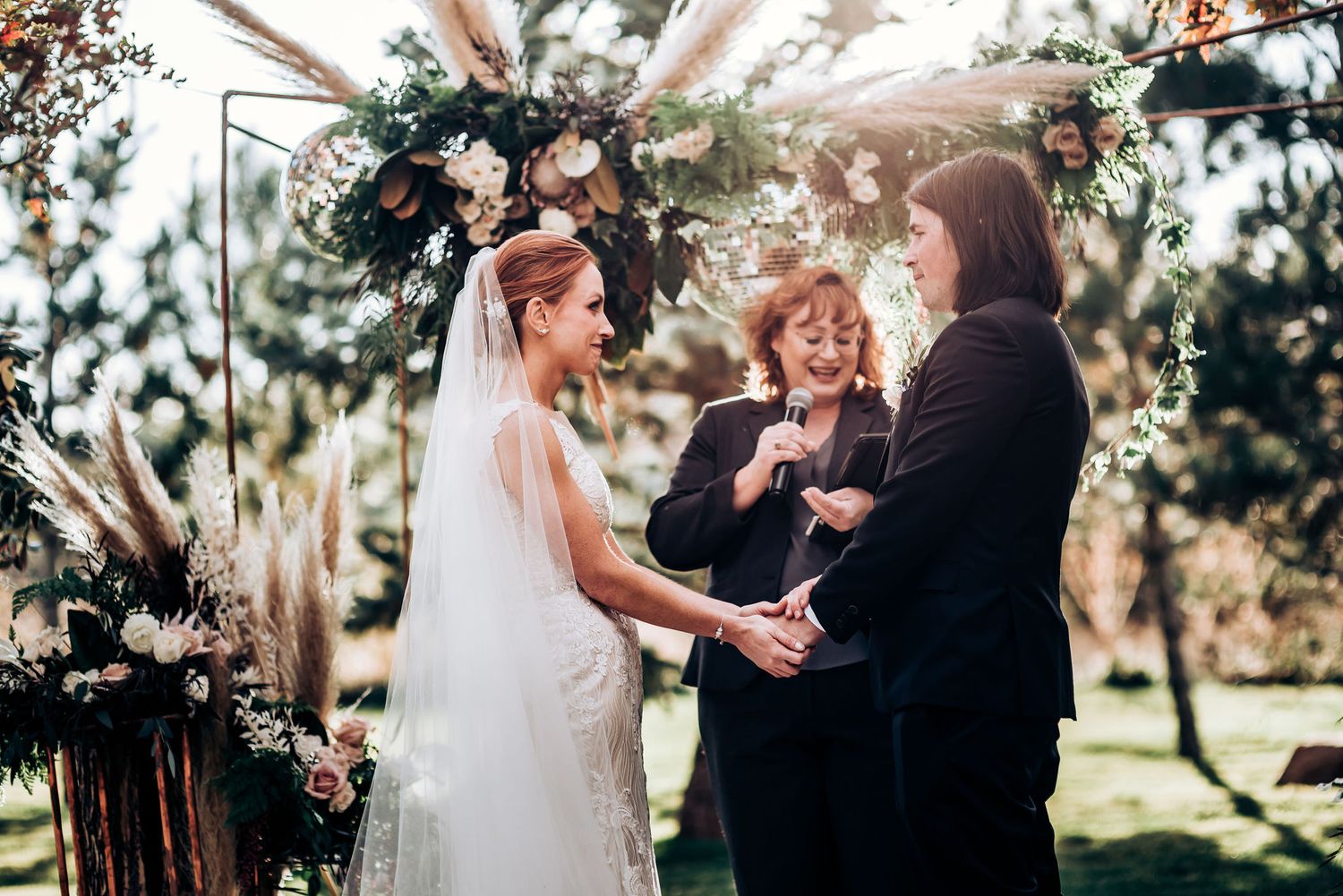 An intimate outdoor wedding ceremony with the couple and officiant under a floral arch.