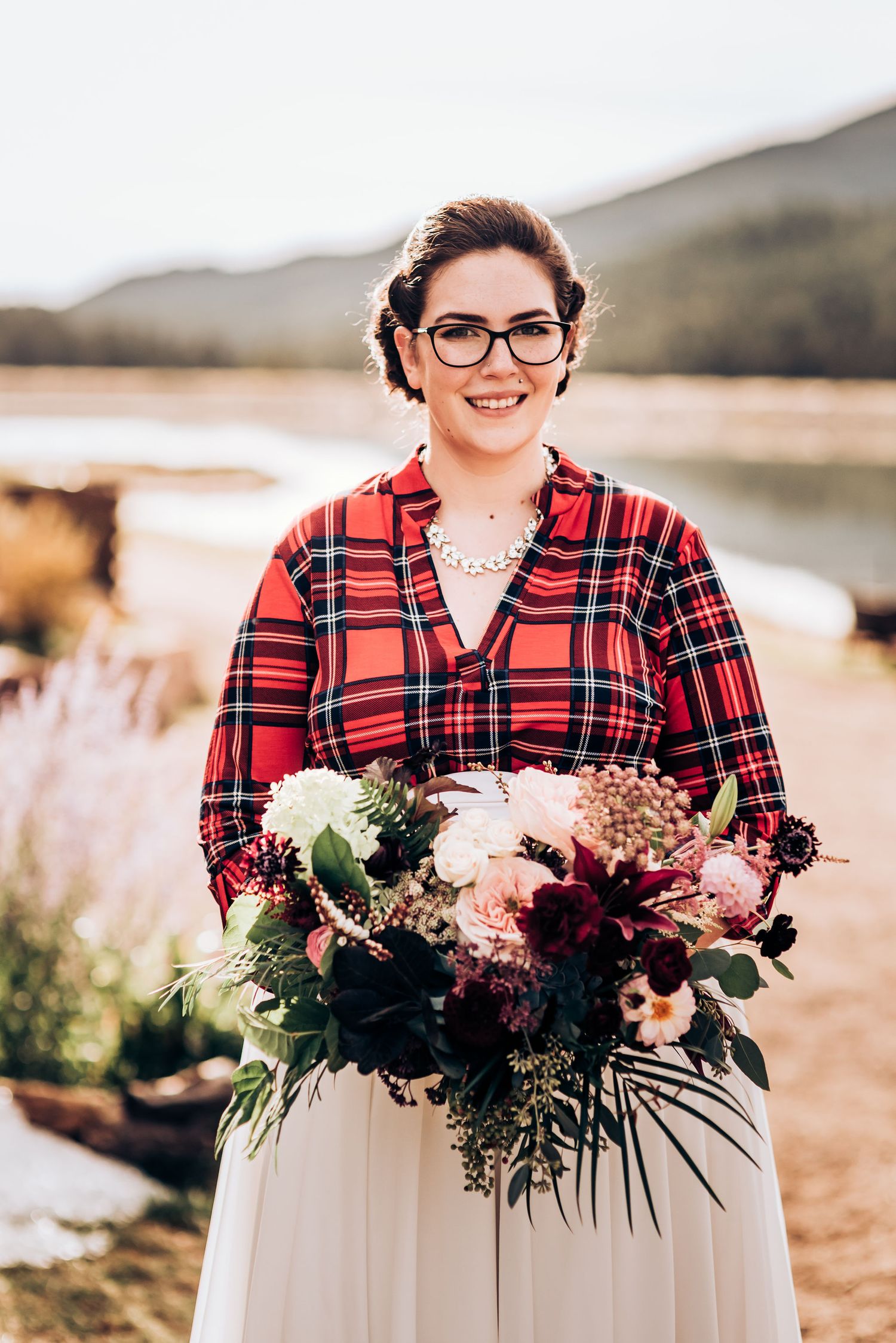 Person in red plaid shirt and glasses holds beautiful bouquet of mixed flowers in outdoor setting.