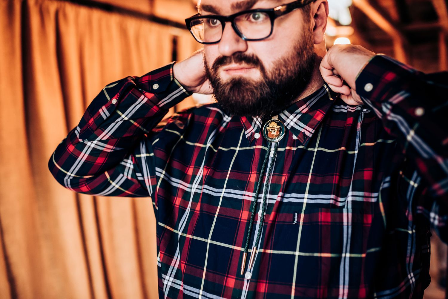Portrait of person wearing glasses and plaid shirt in warm interior lighting.
