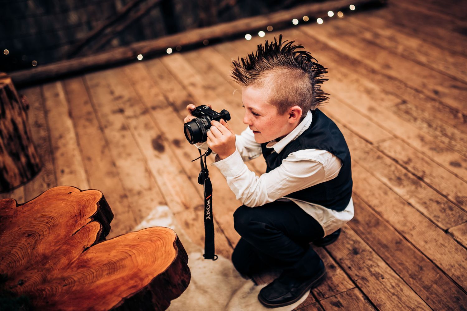 Young photographer in formal wear crouches to capture shots at an event.