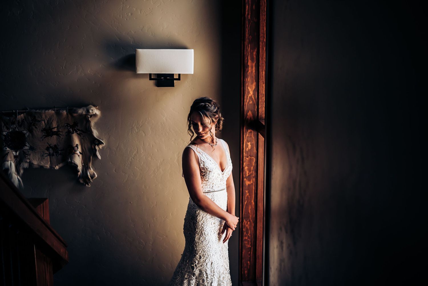 Elegant lace wedding dress silhouette against dark moody wall with window light.