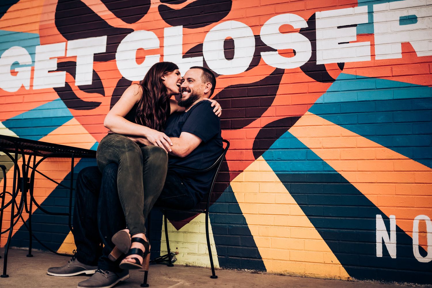 A couple sits intimately against a colorful wall with text reading 'GET CLOSER'.