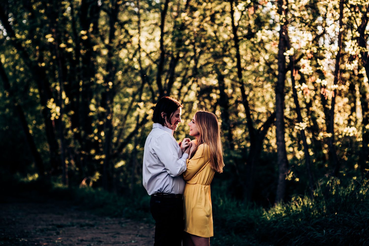 A couple embraces in a sunlit forest wearing yellow dress and white shirt.