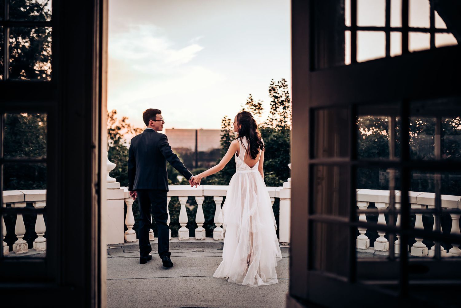Silhouetted wedding couple on classic balcony through doorframe at dusk.